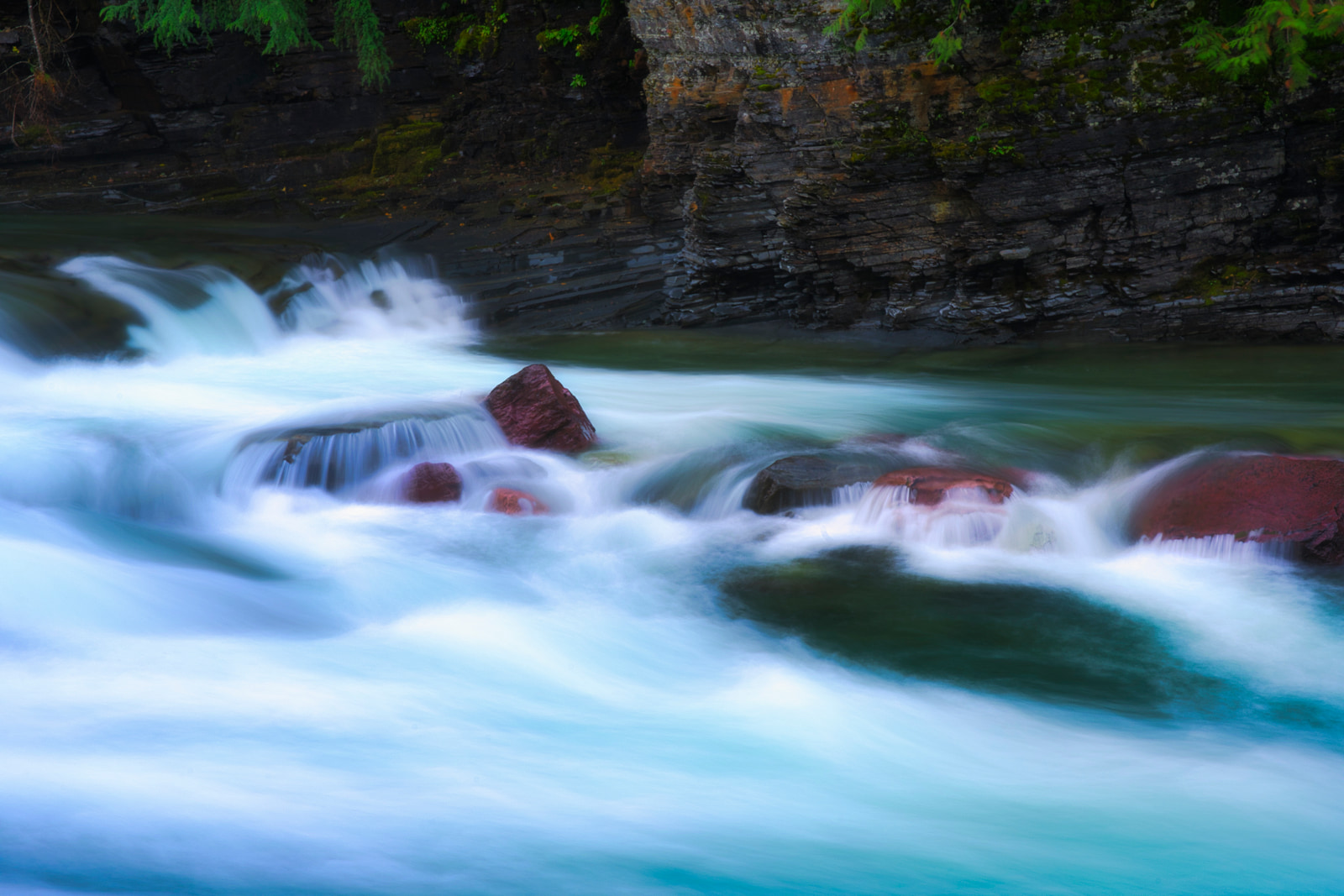 A fast-flowing river cascades over smooth rocks, creating white foam and turquoise water.