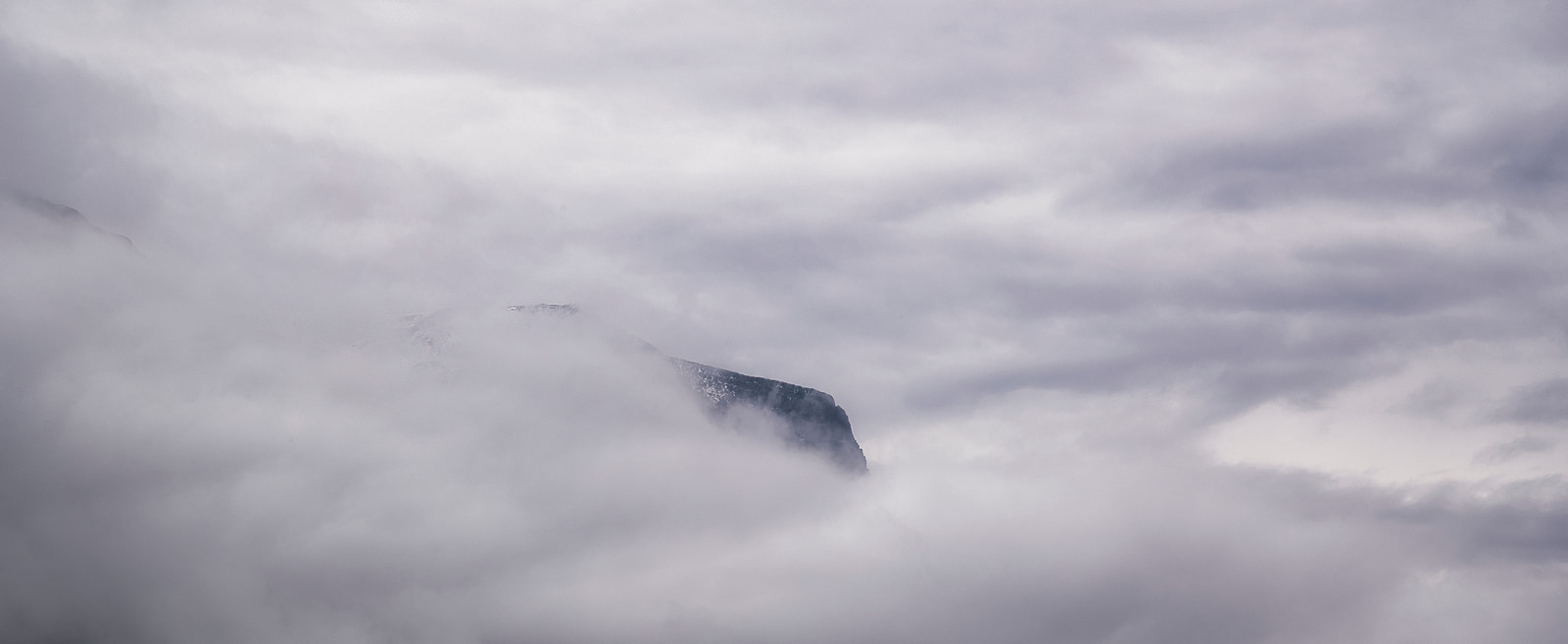 A mountain peak rises sharply through thick, low-hanging clouds.