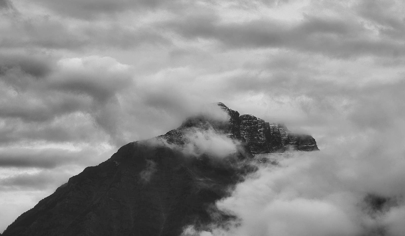 A mountain peak rises above a sea of clouds under a dramatic sky.