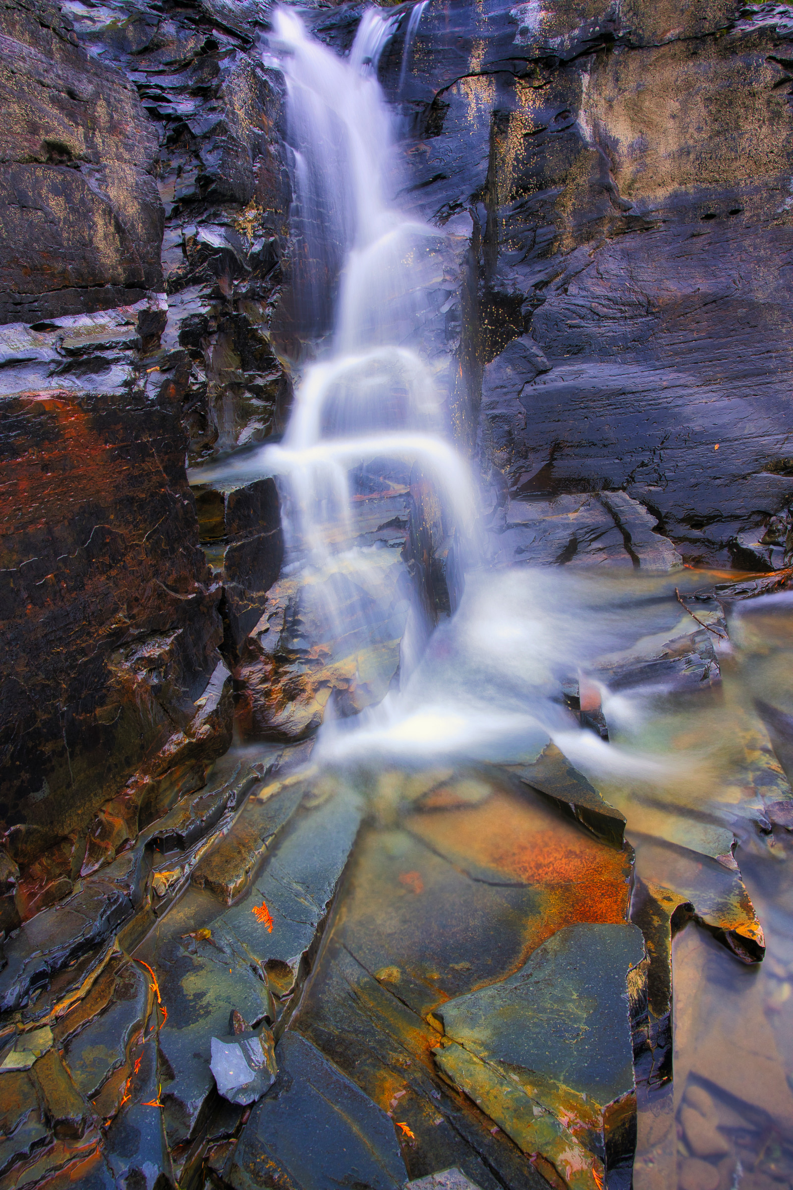 A waterfall cascades over dark, textured rocks, creating a misty spray against a backdrop of rugged stone formations.