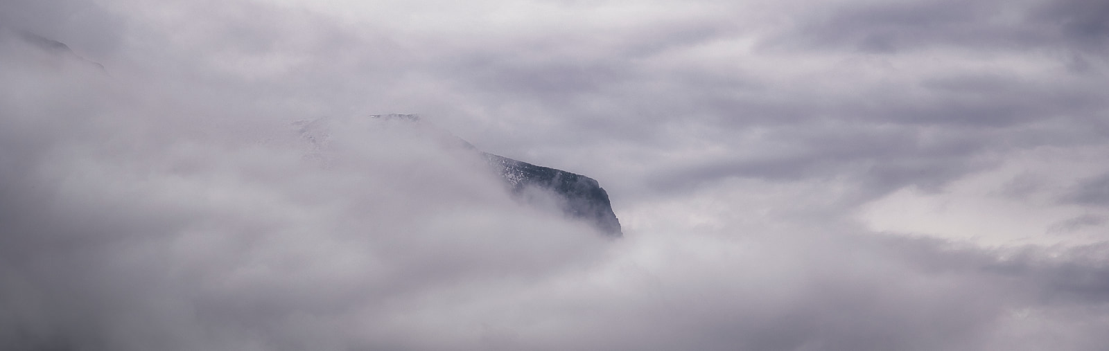 A mountain peak rises sharply through thick, low-hanging clouds.