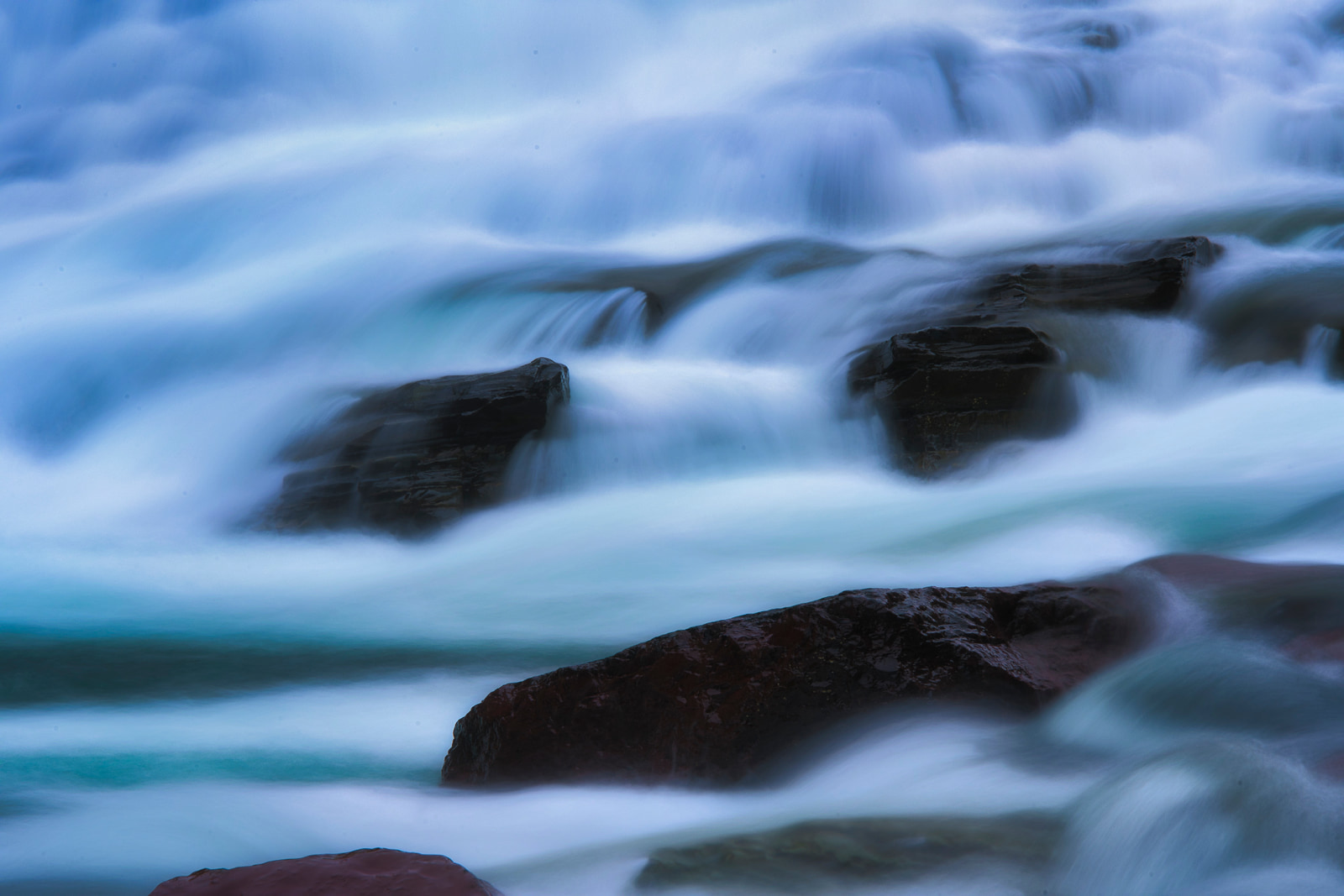 Rapid water flows over dark rocks in a blurred motion.