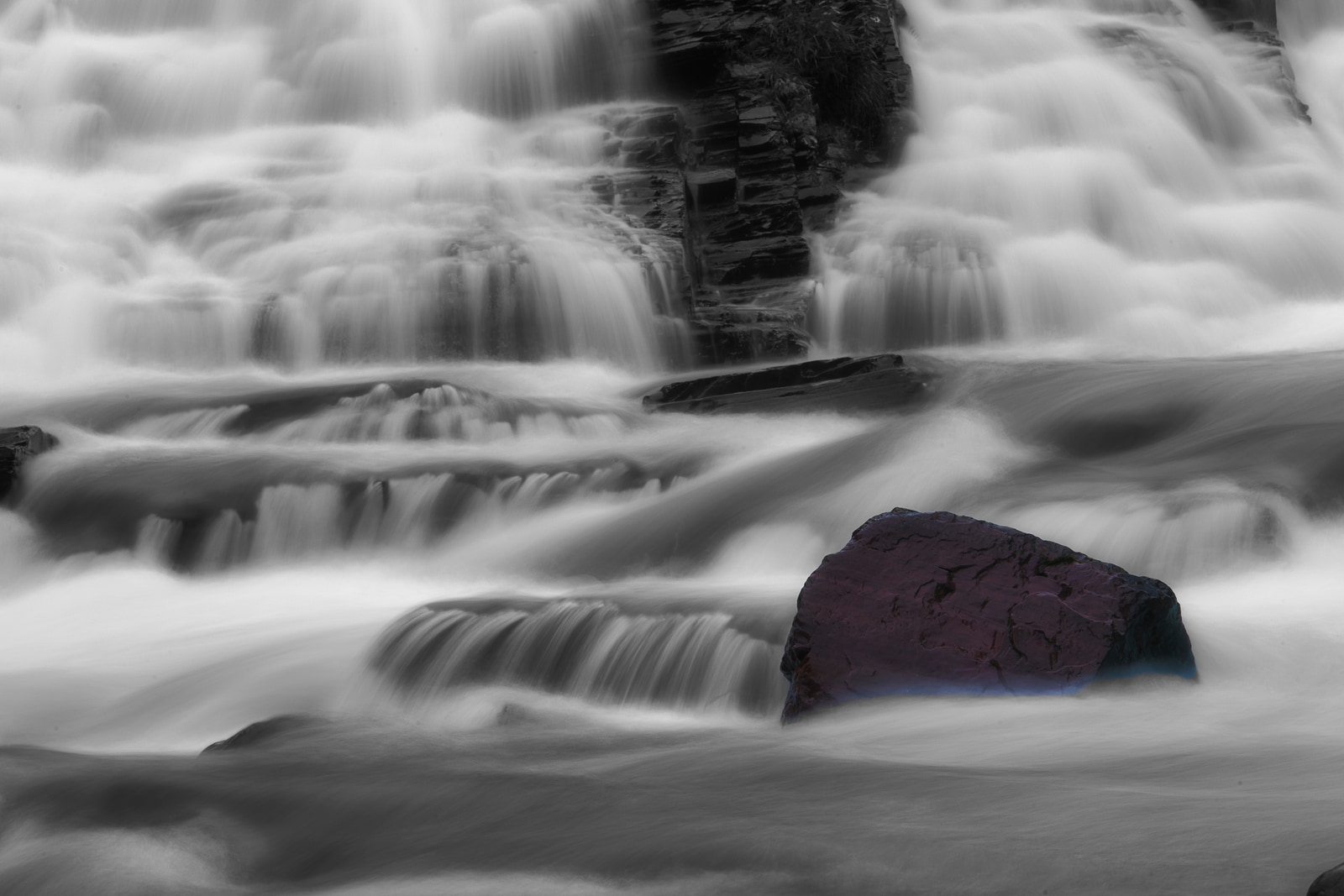 A powerful waterfall cascades over rocky ledges, its frothy white water contrasting with dark stone.