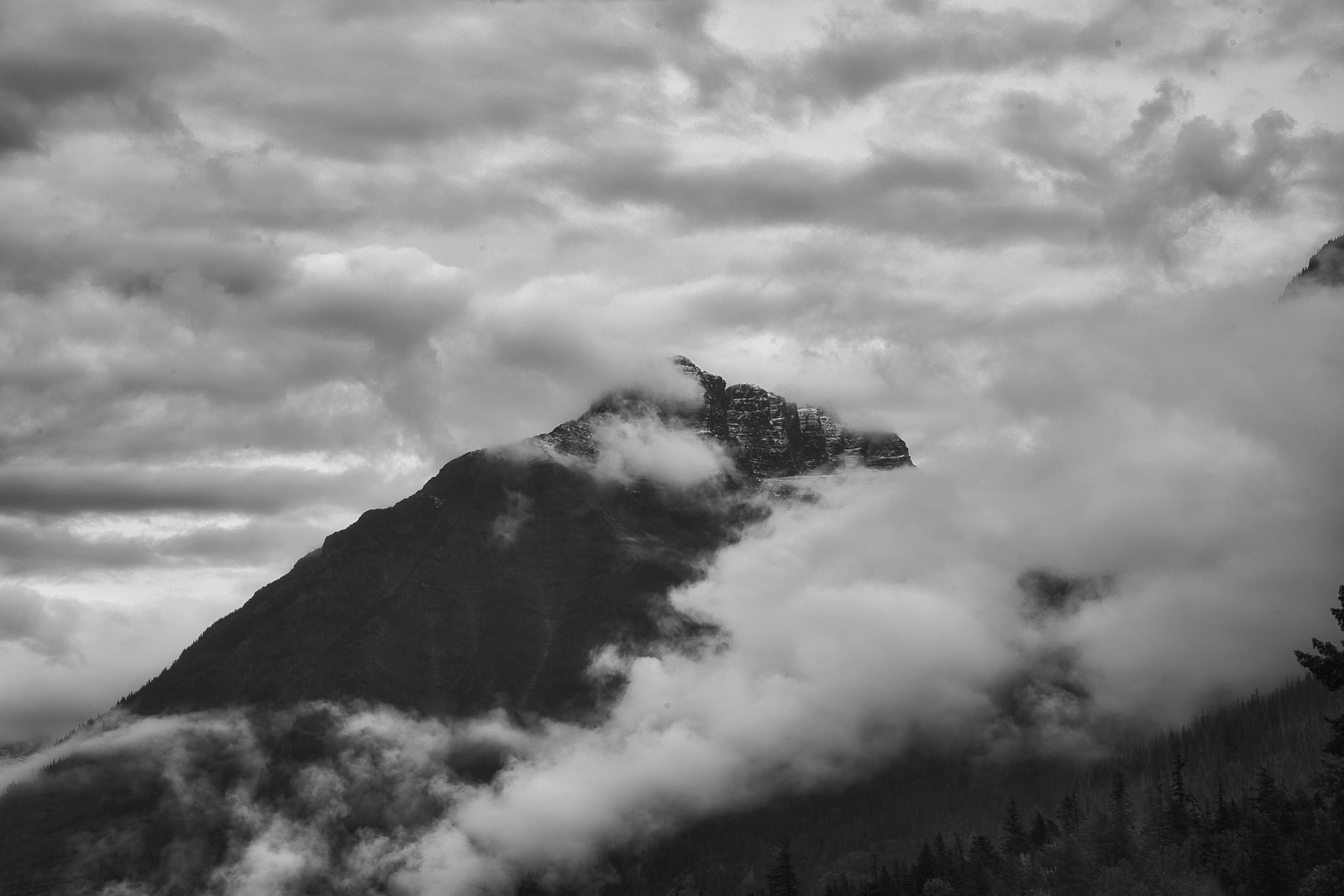 A mountain peak rises above a sea of clouds, its rugged silhouette stark against the overcast sky.